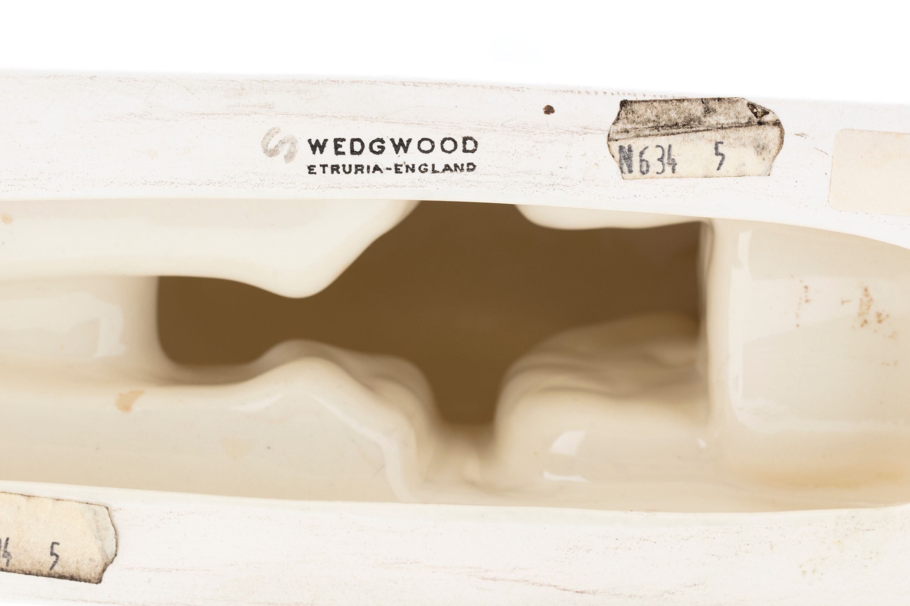 Underside of a white earthenware figure showing the printed black text ‘WEDGWOOD / ETRURIA-ENGLAND’.